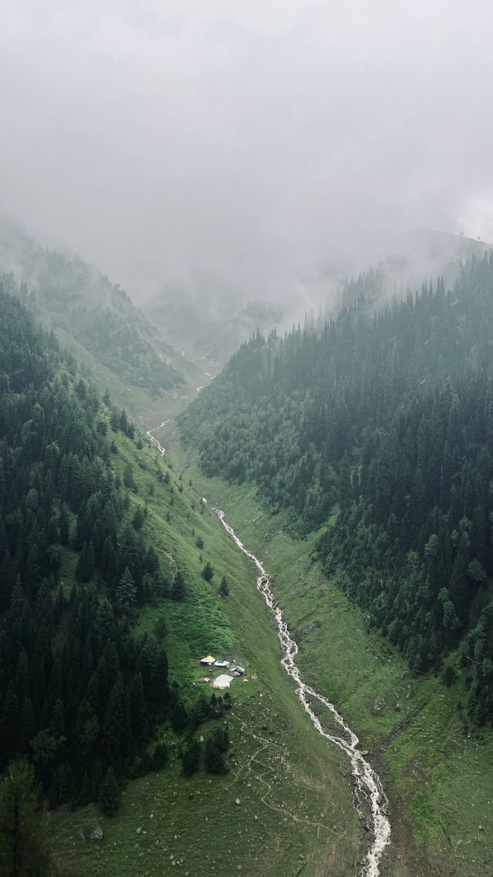 Aerial view of a lush mountain valley with a flowing stream and misty forested hills.